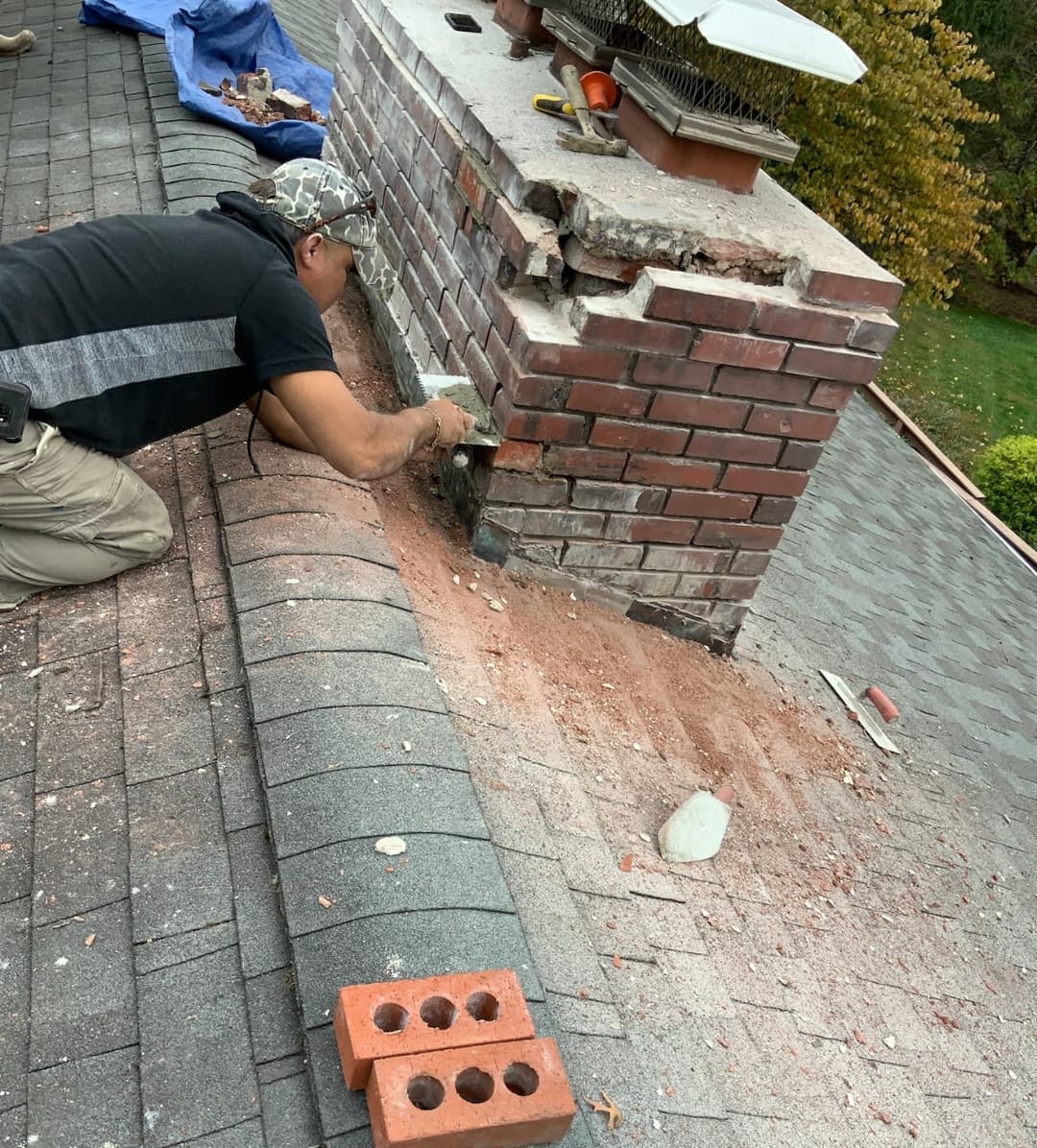Roofer repairing a brick chimney on a house roof with tools and masonry materials.