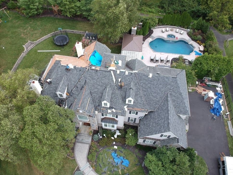 Aerial view of a house with a new roof installation, pool, and backyard features.