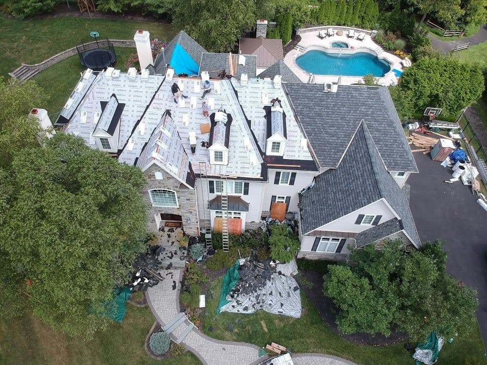 Roofing renovation in progress on a large home, with materials and equipment visible outside.