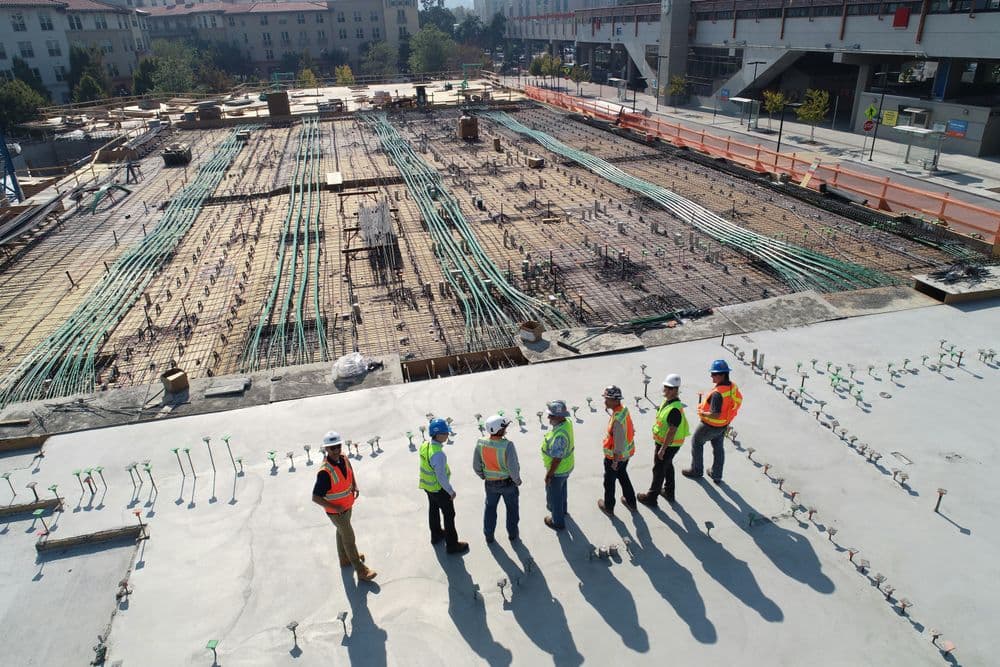 Construction site featuring workers in helmets overseeing foundational work and rebar placement.